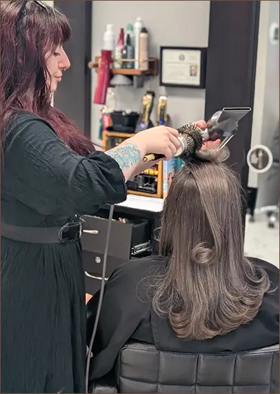 A hairstylist uses a round brush and blow dryer to style a client's shoulder-length hair in a salon. - Pflugerville, TX