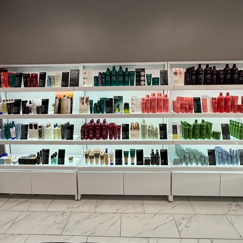 Shelves stocked with various hair care products in bottles and tubes, organized by color and type, in a well-lit retail display against a gray wall. - Pflugerville, TX