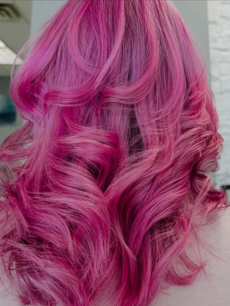 Person with long, wavy, vibrant pink and purple hair, shown from the back against a neutral indoor background. - Pflugerville, TX